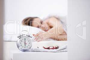 Waking from her slumber. A young woman waking up and reaching over to her alarm clock.