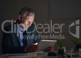 Working late made worthwhile. Shot of a mature businessman using a digital tablet while working late in an office.