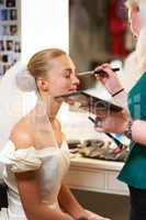 Making sure she looks perfect. A make-up artist applying make-up to a bride.