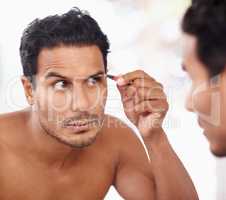 He takes grooming to the next level. A young man plucking his eyebrows while looking in the mirror.