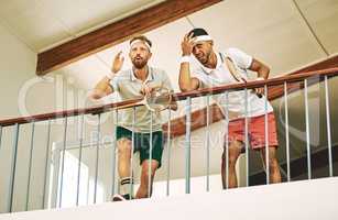 If you blink youll miss it. Shot of two young men watching a game of squash from the viewing gallery.