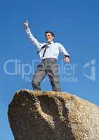 Moving up in his career. A young businessman standing with his arms raised in victory atop a cliff.