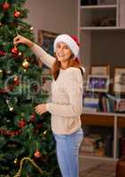 Filling my home with holiday happiness. Shot of a beautiful young woman decorating her Christmas tree at home.