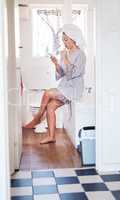 Sending a quick text while freshening up. Shot of a young woman using her cellphone while brushing her teeth in the bathroom.