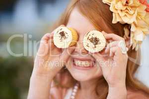 Looking sweet. A little girl playfully holding cupcakes in front of her eyes.