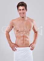 Like what you see. Studio shot of a bare-chested young man with a towel wrapped around his waist.
