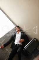 Completely and utterly exhausted. Shot of an exhausted young businessman lying on the floor beside his luggage.