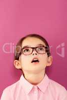 Childlike wonder. A little girl wearing spectacles looking up against a pink background.