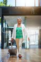 On her way to see the world. Shot of a mature woman walking in an airport terminal with her suitcase.