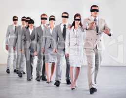 Business without strategy is chaos. Shot of a group of blindfolded businesspeople following their equally blind manager.