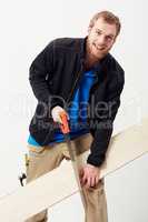 Casual carpenter. Portrait of a young carpenter sawing a piece of wood against his leg.