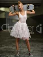 Dainty yet daring. A young ballerina holding a skateboard while wearing a tutu and sneakers.