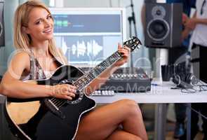 This song is going to be a hit. A gorgeous blonde guitarist sitting in a recording studio with her instrument.