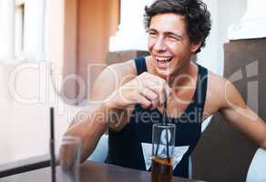 That joke was hilarious. Handsome young guy laughing while enjoying his cold beverage.