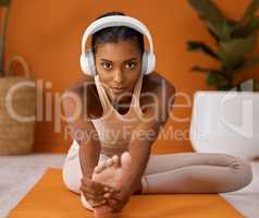 The right tunes set the mood for a workout. Shot of a young woman stretching during a yoga routine against a studio background.