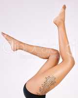 Smooth and effortless. Cropped shot of an unrecognizable womans tattooed legs in studio against a grey background.