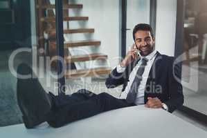 Business just went from good to great. Shot of a handsome young businessman relaxing with his feet up on an office desk while using his phone.