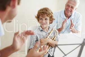 Supporting his talent. Shot of a cute little boy looking pleased as his father and grandfather cheer him on after playing the trumpet.