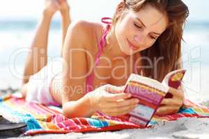 Beautiful young woman reading book on beach. Beautiful young woman lying and reading book on the sea shore.
