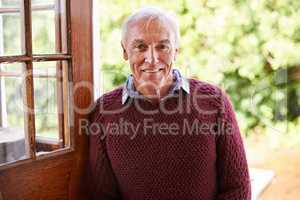 Invite an old man inside. Portrait of a happy senior man leaning against the doorway to his home.