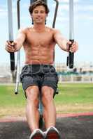 Taking fitness outdoors. Smiling and handsome young man working out using outdoor exercise equipment.