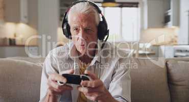 Ooo, the opponents getting close. Shot of a senior man sitting alone on the sofa at home and wearing headsets while gaming.