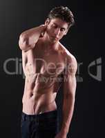 Lean and bulky. Studio shot of a handsome bare-chested young athlete standing against a black background.