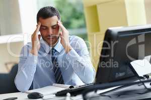 My head is killing me. A stressed young businessman sitting at his desk and struggling with a bad headache.