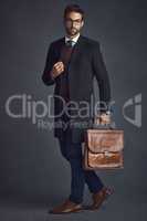 Style thats good to go. Studio shot of a stylishly dressed young man carrying a bag against a gray background.