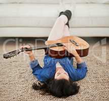 The perfect way to unwind. Shot of a young woman playing the guitar while lying on her living room floor.