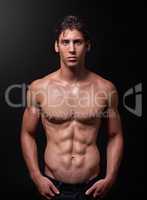 Herculean hunk. Studio shot of a handsome bare-chested young athlete standing against a black background.