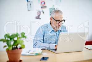 Shot of a handsome businessman working on his laptop. The commercial designs displayed in this image represent a simulation of a real product and have been changed or altered enough by our team of retouching and design specialists so that they are free of