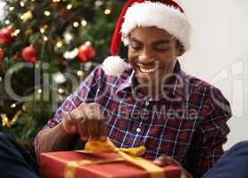 Christmas is my favourite time of year. Shot of a handsome young man unwrapping his Christmas present.