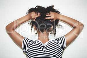 Embrace the curl. Rearview studio shot of a woman lifting the hair off of her neck against a gray background.