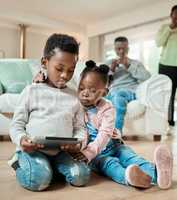 Shes always interested on what her brothers doing. Full length shot of young boy and his adorable little sister using a tablet while sitting on the living room floor at home.