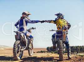 Time to rip up this track. Two motocross riders bumping fists before a race.