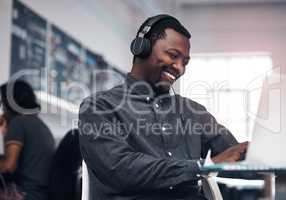 Music makes work so much enjoyable. Cropped shot of a handsome young businessman using a laptop while wearing headphones in a modern office.