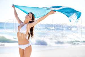 Carefree in the summer breeze. Portrait of a beautiful young woman holding a sarong thats blowing in the wind.