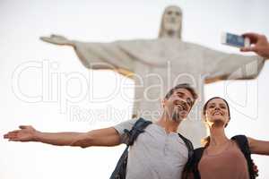 Take one while we pose. Shot of a happy young couple taking photos at the Christ the Redeemer statue.
