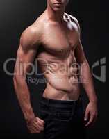 More muscle, more man. Studio shot of a handsome bare-chested young athlete standing against a black background.