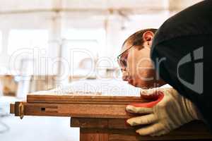 I like having a dust-free working environment. Shot of a handsome young carpenter blowing dust off a wooden plank inside a workshop.