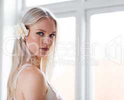 Beauty and pureness. Portrait of an attractive woman with a white rose in her hair while standing in her bedroom.