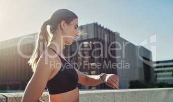 Time and commitment, the best ingredients for progress. Shot of a young woman looking at her watch while exercising in the city.