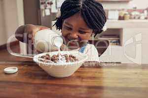 I like my breakfasts very milky. Cropped shot of an adorable little girl pouring milk into her cereal bowl at home.