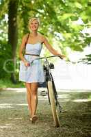 Out for a leisurely ride. Pretty young woman walking through a tree-lined country path while pushing her bicycle.