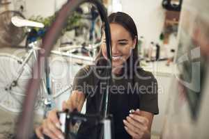 This repair was quicker than I expected. Shot of an attractive young woman standing alone in her shop and repairing a bicycle wheel.