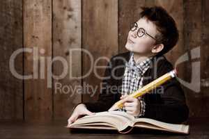 Writing down some big ideas. Young boy wearing glasses and doing his homework with an enormous pencil.