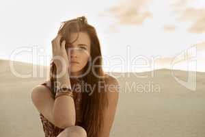 Freedom and isolation on the beach. Shot of a beautiful young fashion model sitting in the sand.