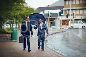 Seeking new opportunities in the city. Shot of two corporate businessmen travelling through the city on a rainy day.