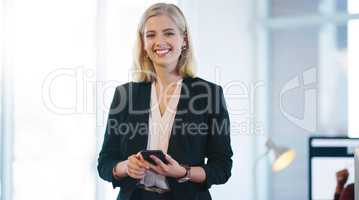 Confidence is what you need to make a company survive. Portrait of a confident young businesswoman holding her cellphone while standing inside of the office.